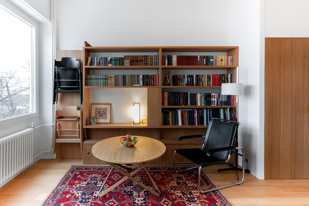 Cette image montre une petite salle de séjour design avec une bibliothèque ou un coin lecture, un mur blanc et un sol en bois brun.