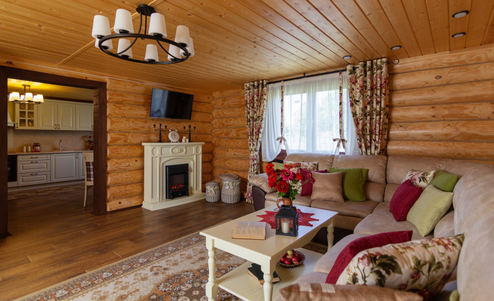Пример оригинального дизайна: гостиная комната в стиле кантри с полом из ламината, стандартным камином, фасадом камина из дерева, телевизором на стене, коричневым полом, потолком из вагонки и деревянными стенами