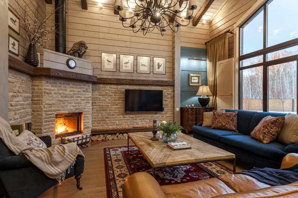 Réalisation d'un salon champêtre ouvert et de taille moyenne avec un mur beige, une cheminée d'angle, un téléviseur fixé au mur, un sol en bois brun, un manteau de cheminée en pierre, un sol marron, poutres apparentes et du lambris.