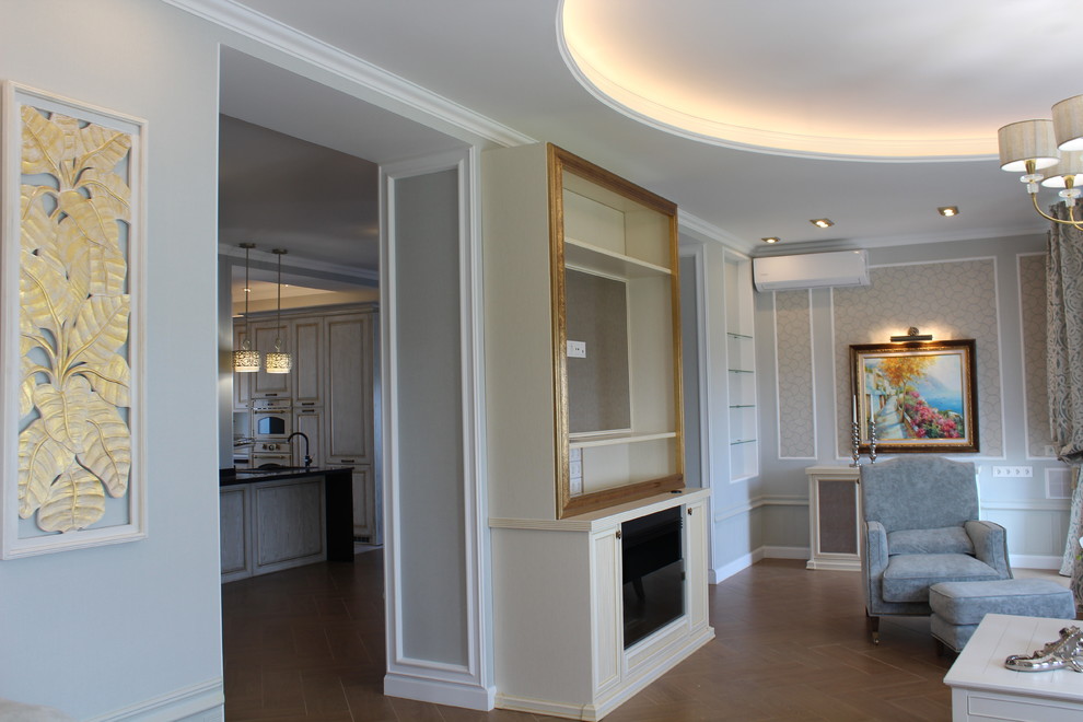 На фото: большая открытая гостиная комната в стиле неоклассика (современная классика) с серыми стенами, полом из керамогранита, подвесным камином, фасадом камина из дерева, телевизором на стене и коричневым полом с