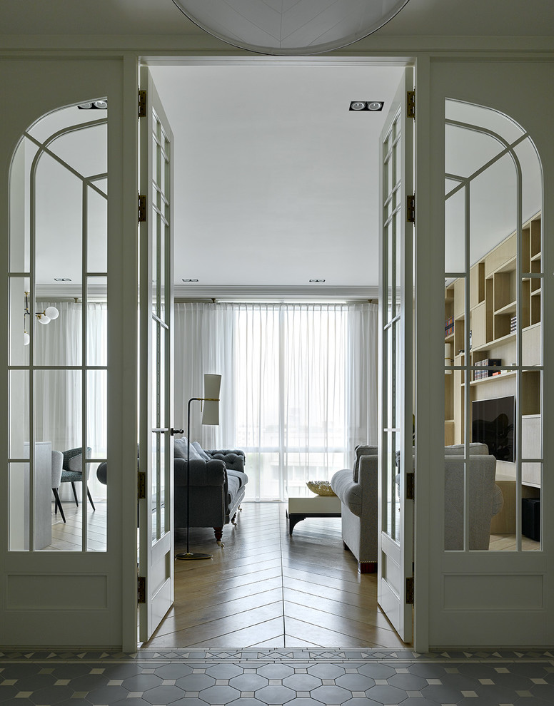 Пример оригинального дизайна: открытая гостиная комната в современном стиле с с книжными шкафами и полками, белыми стенами, светлым паркетным полом, телевизором на стене и бежевым полом