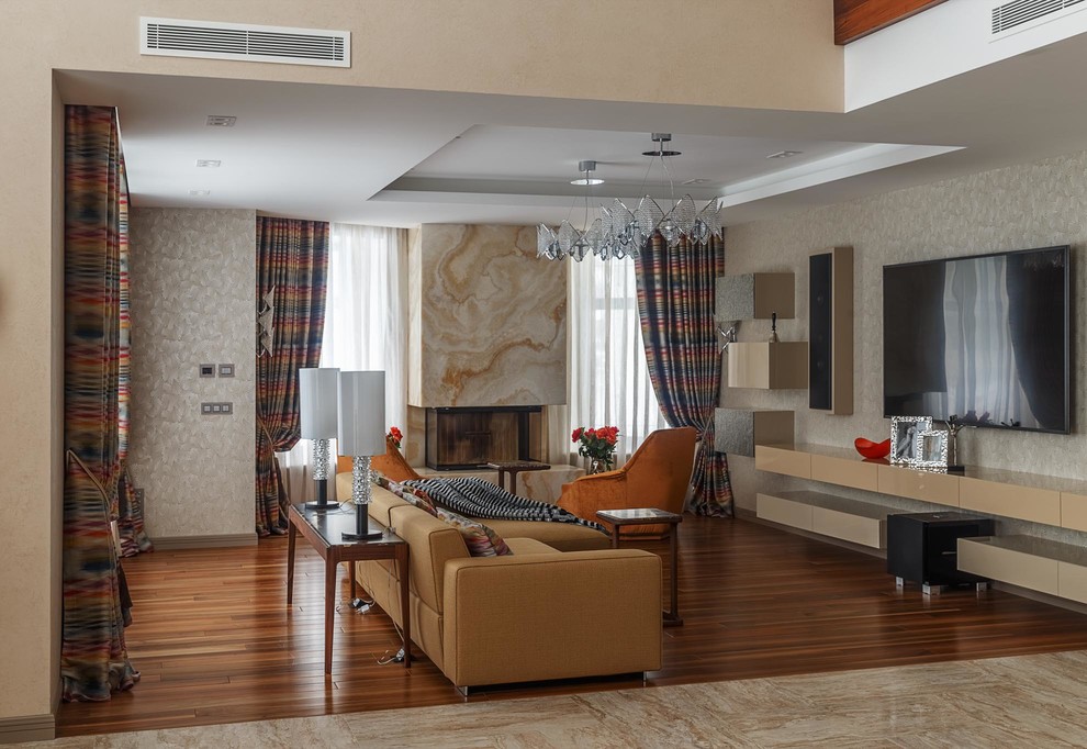 Идея дизайна: большая гостиная комната в современном стиле с бежевыми стенами, телевизором на стене, паркетным полом среднего тона, стандартным камином, фасадом камина из камня, коричневым полом и коричневым диваном