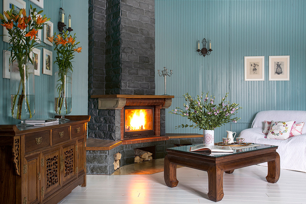 Idee per un soggiorno eclettico con pareti blu, pavimento in legno verniciato, camino ad angolo e cornice del camino in pietra