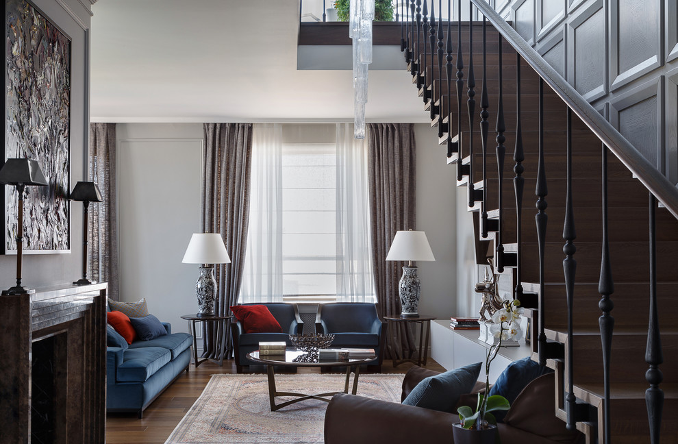 На фото: гостиная комната в стиле неоклассика (современная классика) с серыми стенами, темным паркетным полом, стандартным камином, коричневым полом и синим диваном с