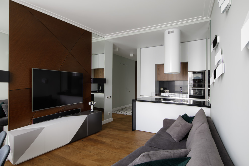 Foto de salón para visitas abierto actual con paredes grises, suelo de madera en tonos medios, televisor colgado en la pared y suelo marrón