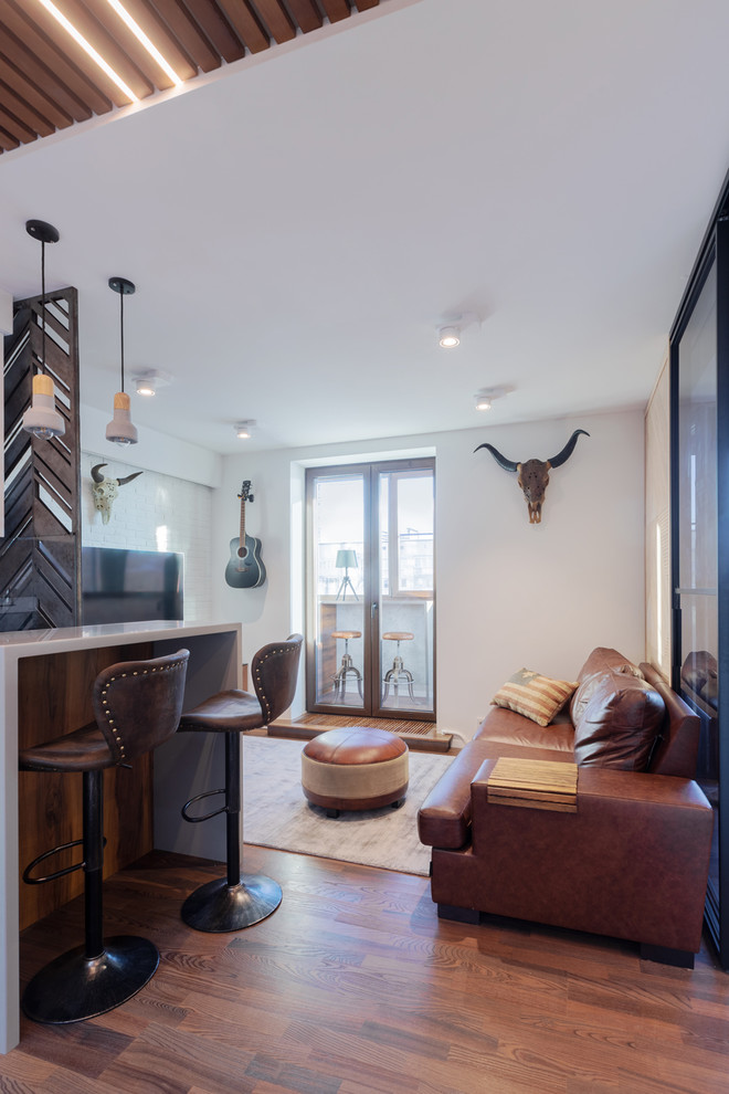 Imagen de salón con barra de bar abierto actual pequeño con paredes blancas, suelo de madera en tonos medios, televisor colgado en la pared y suelo marrón