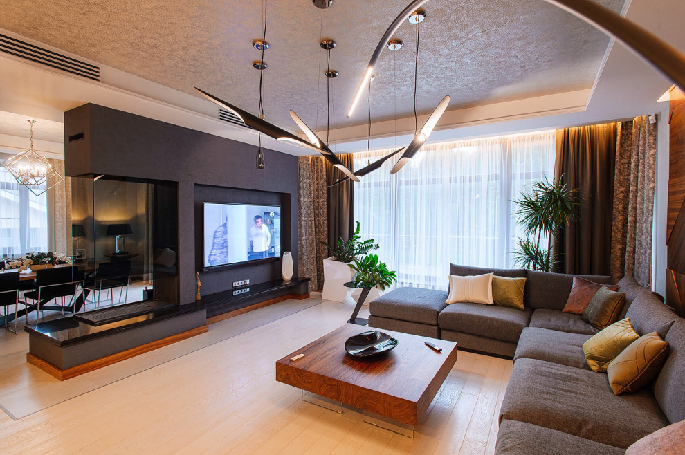 Ejemplo de salón actual grande con paredes blancas, suelo de madera clara, chimenea de doble cara, televisor colgado en la pared y suelo beige
