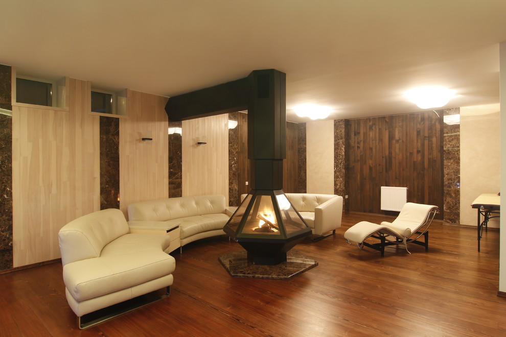 Cette image montre un grand salon bohème ouvert avec un bar de salon, un mur blanc, parquet clair, une cheminée standard, un manteau de cheminée en pierre, un téléviseur fixé au mur et un sol beige.