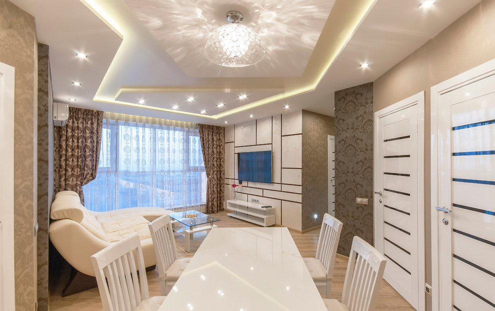 Стильный дизайн: гостиная комната среднего размера в современном стиле с бежевыми стенами, полом из ламината и телевизором на стене - последний тренд