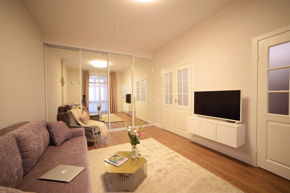 Пример оригинального дизайна: гостиная комната среднего размера в современном стиле с бежевыми стенами, полом из ламината, телевизором на стене и бежевым полом
