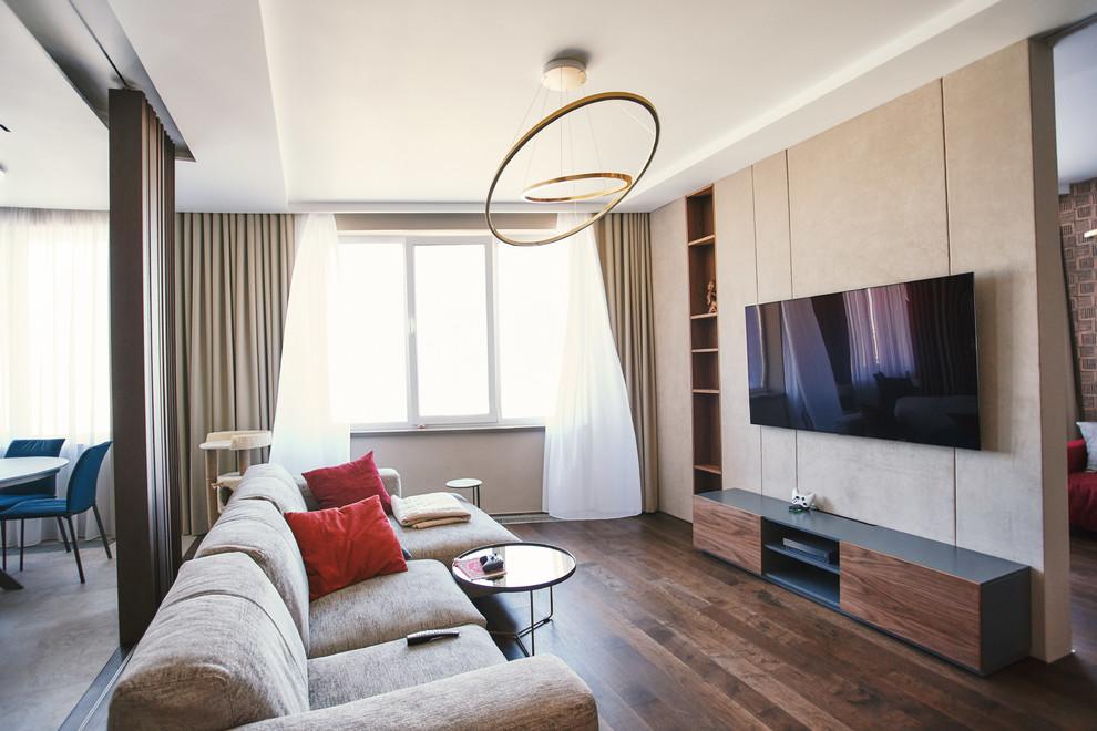 На фото: открытая, объединенная гостиная комната в современном стиле с бежевыми стенами, темным паркетным полом, телевизором на стене и коричневым полом