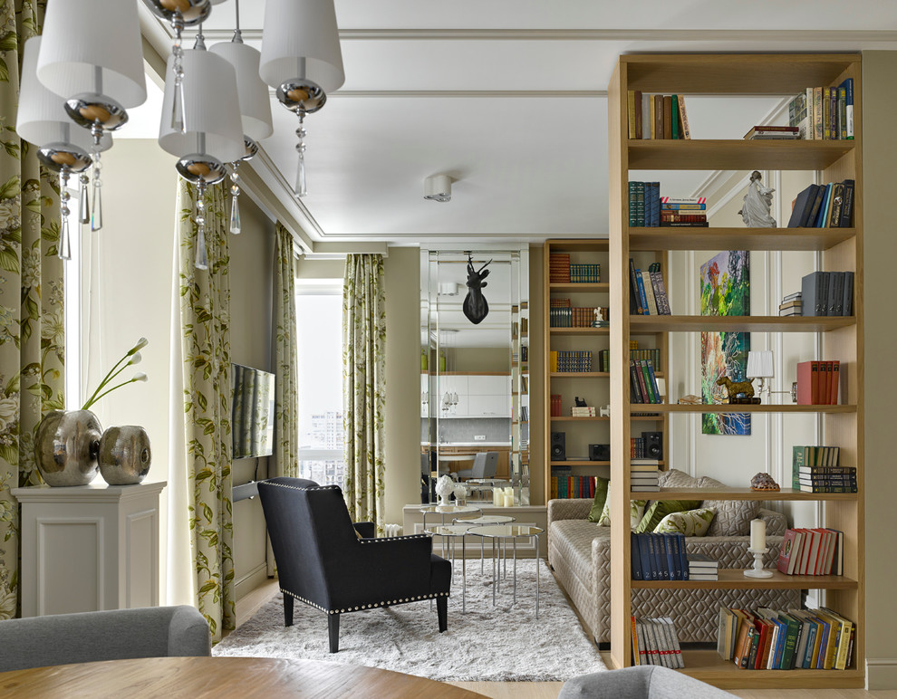На фото: открытая гостиная комната в стиле фьюжн с с книжными шкафами и полками, бежевыми стенами и телевизором на стене с
