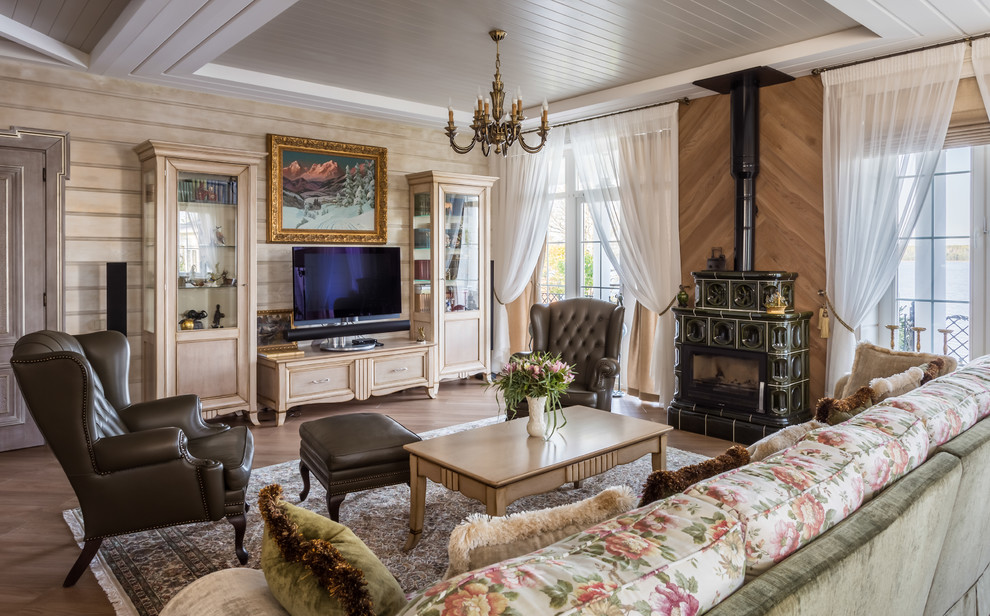 На фото: большая гостиная комната в классическом стиле с бежевыми стенами, печью-буржуйкой, коричневым полом и ковром на полу с