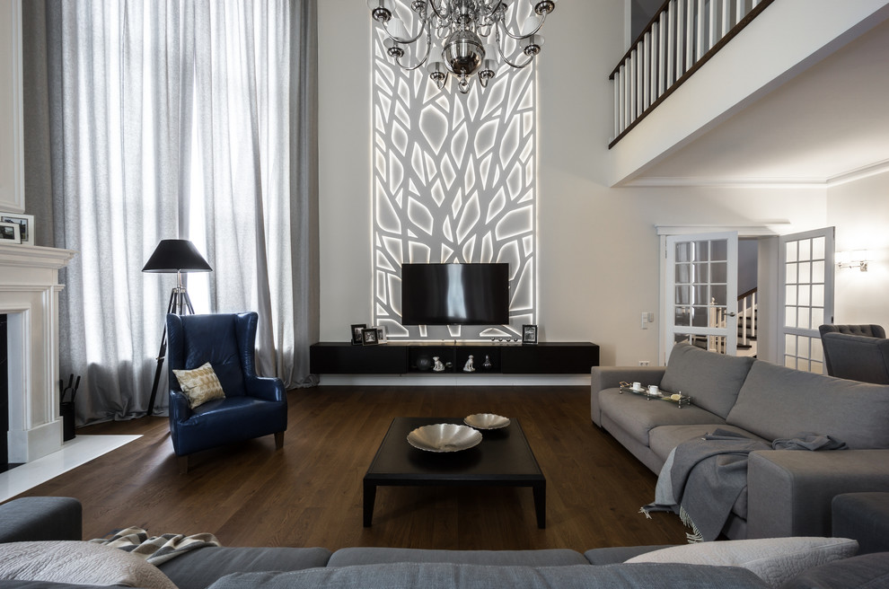 На фото: большая объединенная гостиная комната:: освещение в стиле неоклассика (современная классика) с белыми стенами, темным паркетным полом, телевизором на стене и коричневым полом