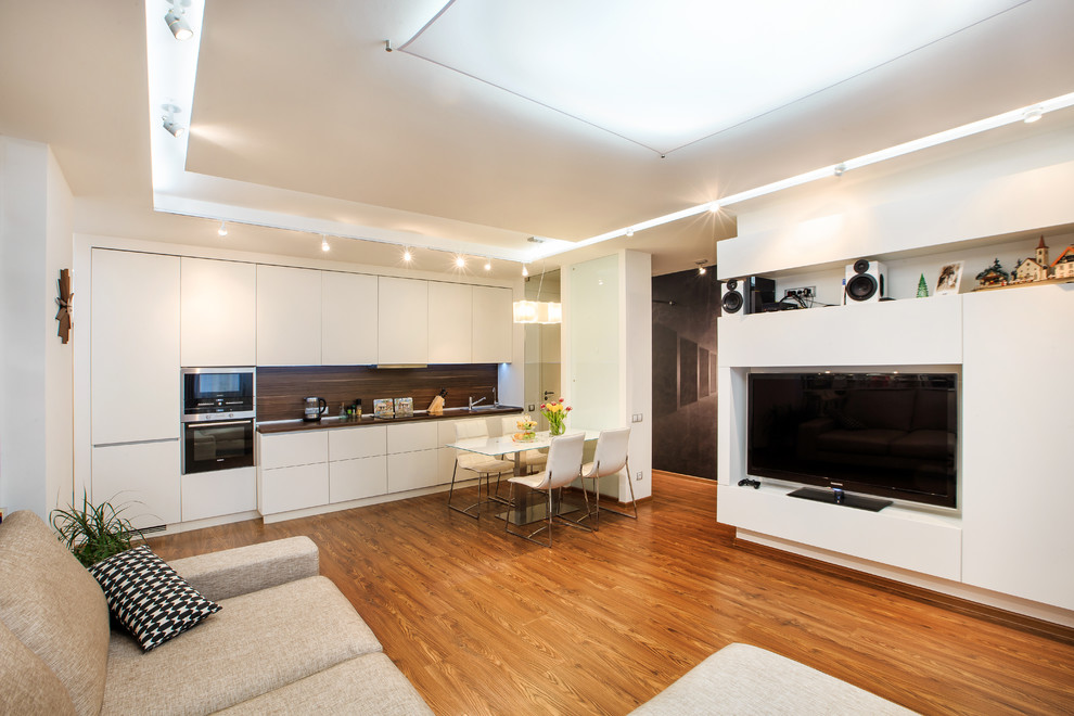 Imagen de salón abierto actual con paredes blancas, suelo de madera en tonos medios y pared multimedia
