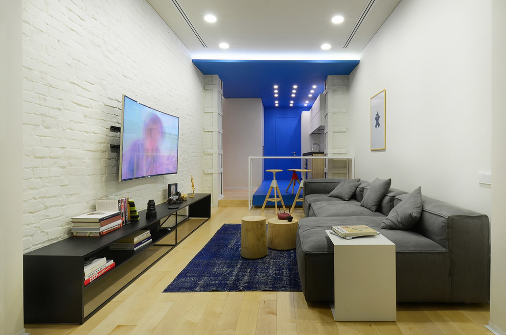 На фото: гостиная комната в современном стиле с белыми стенами, светлым паркетным полом и телевизором на стене без камина