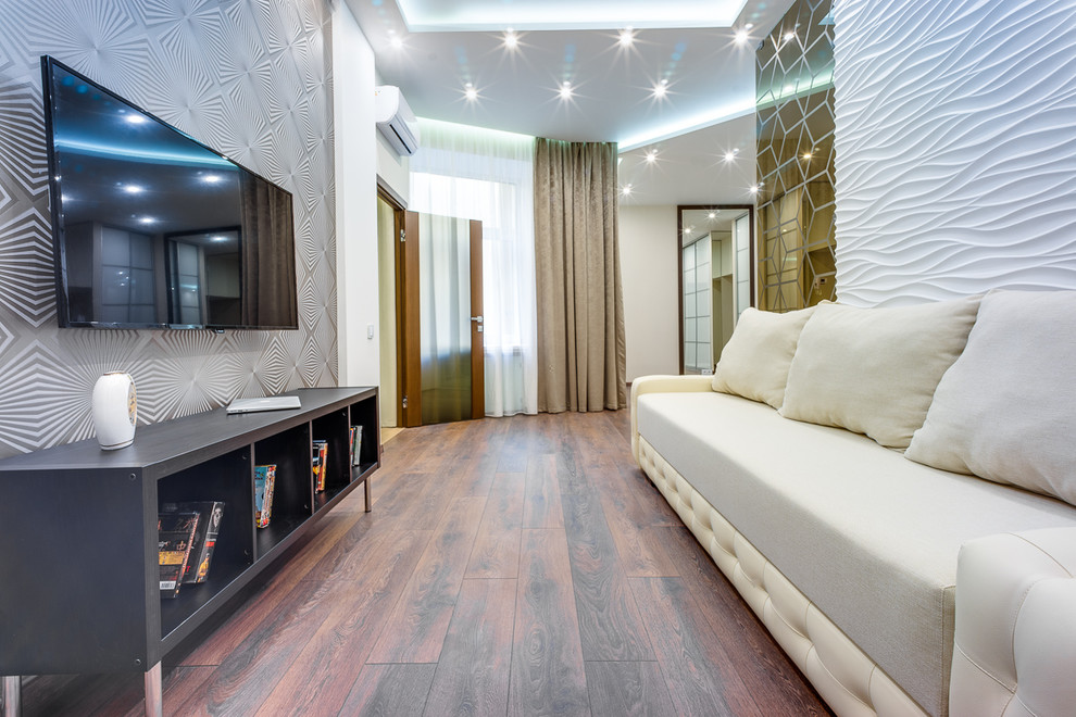 Свежая идея для дизайна: открытая гостиная комната среднего размера в современном стиле с бежевыми стенами, полом из ламината, телевизором на стене и коричневым полом - отличное фото интерьера