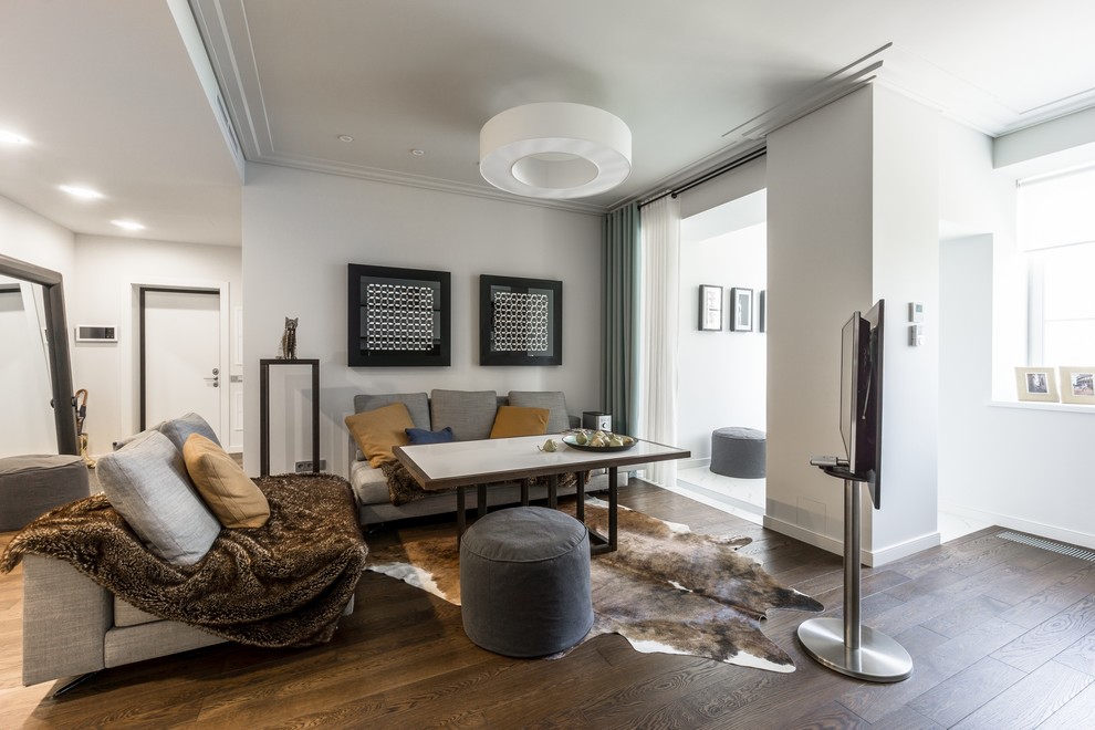 Стильный дизайн: открытая гостиная комната в современном стиле с белыми стенами, темным паркетным полом и отдельно стоящим телевизором - последний тренд