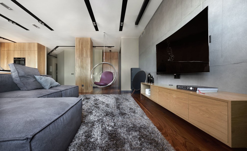 Modelo de salón abierto actual con paredes grises, suelo de madera oscura, televisor colgado en la pared y suelo marrón