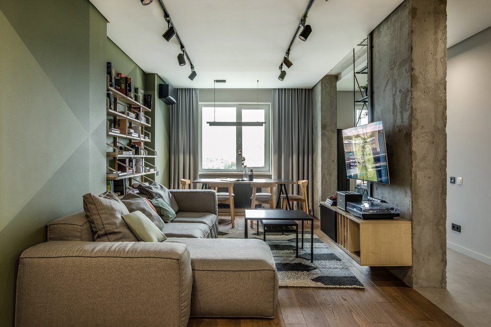 Ispirazione per un soggiorno design di medie dimensioni e aperto con libreria, pareti verdi, pavimento in legno massello medio e TV a parete