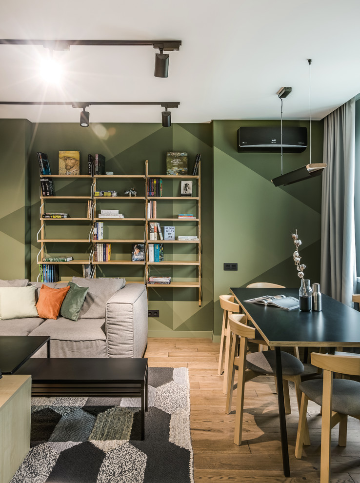 Cette image montre un salon design de taille moyenne et ouvert avec une bibliothèque ou un coin lecture, un mur vert, un sol en bois brun et un téléviseur fixé au mur.
