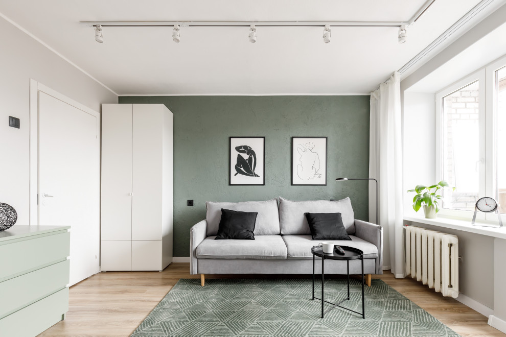 Стильный дизайн: маленькая открытая, объединенная гостиная комната в современном стиле с зелеными стенами, полом из ламината, отдельно стоящим телевизором и коричневым полом для на участке и в саду - последний тренд