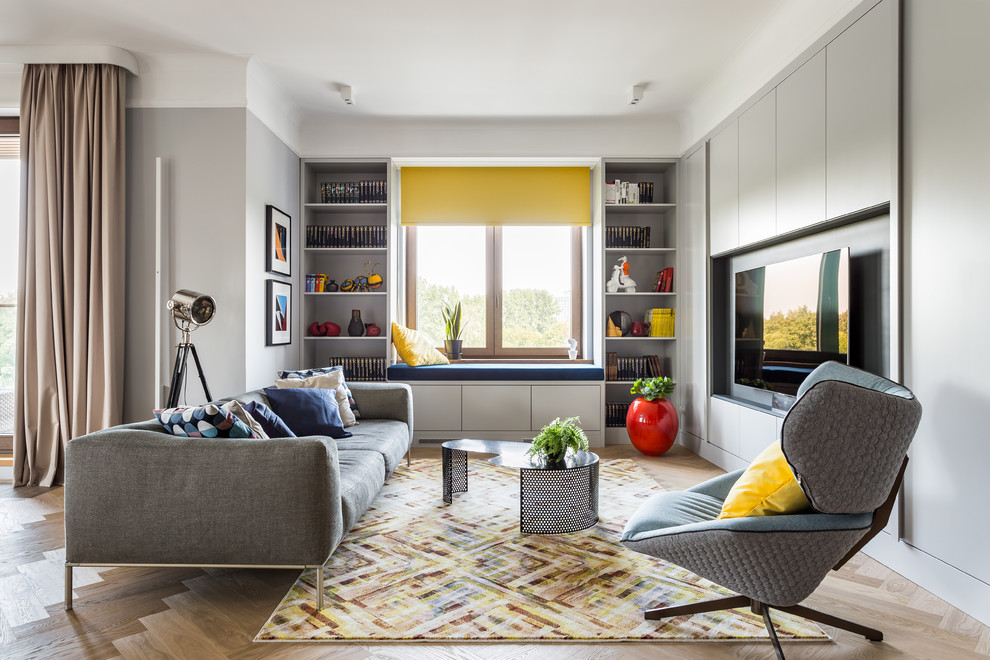 Modelo de sala de estar con biblioteca abierta contemporánea de tamaño medio sin chimenea con paredes grises, suelo beige, suelo de madera clara y pared multimedia