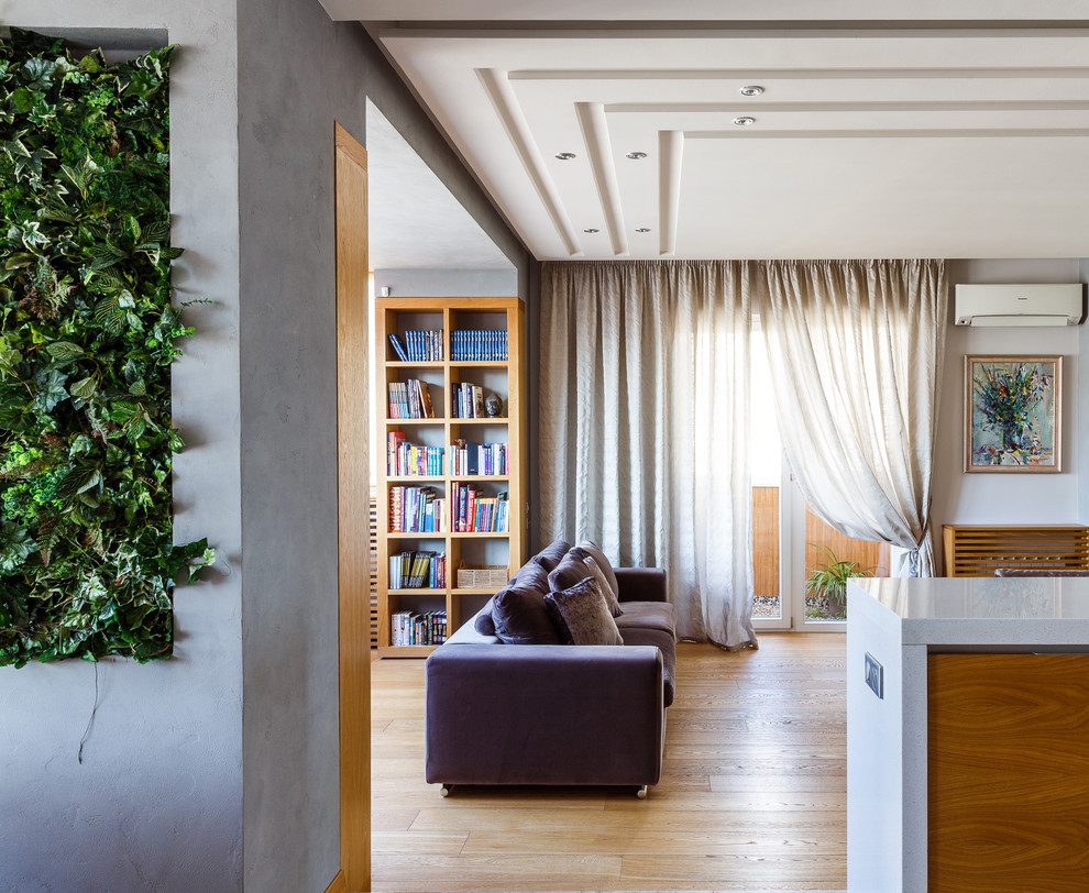 Ispirazione per un soggiorno design di medie dimensioni e aperto con libreria, pareti bianche, parquet chiaro e pavimento beige