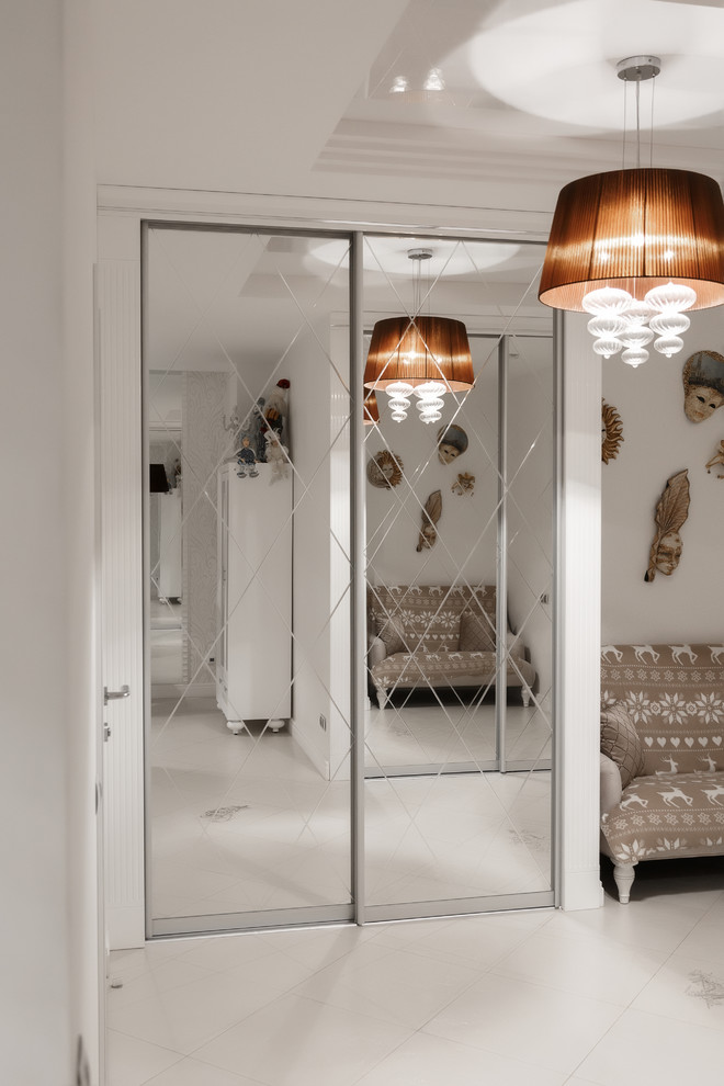 Идея дизайна: открытая гостиная комната среднего размера в стиле неоклассика (современная классика) с с книжными шкафами и полками, белыми стенами, полом из керамогранита, телевизором на стене и белым полом без камина