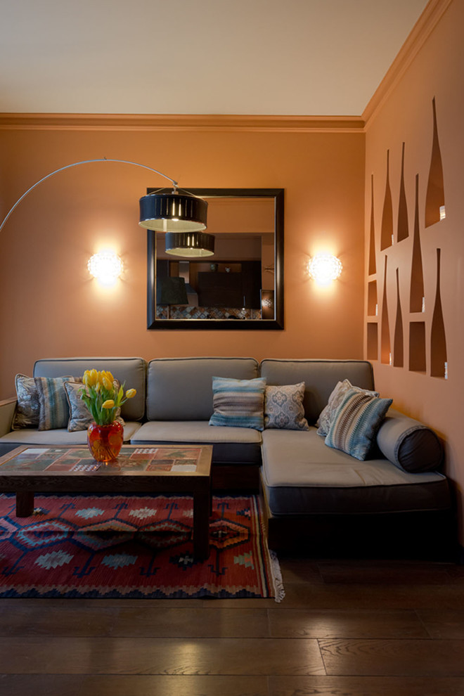 Cette image montre un salon bohème de taille moyenne et ouvert avec un mur orange, un sol en bois brun et un téléviseur fixé au mur.