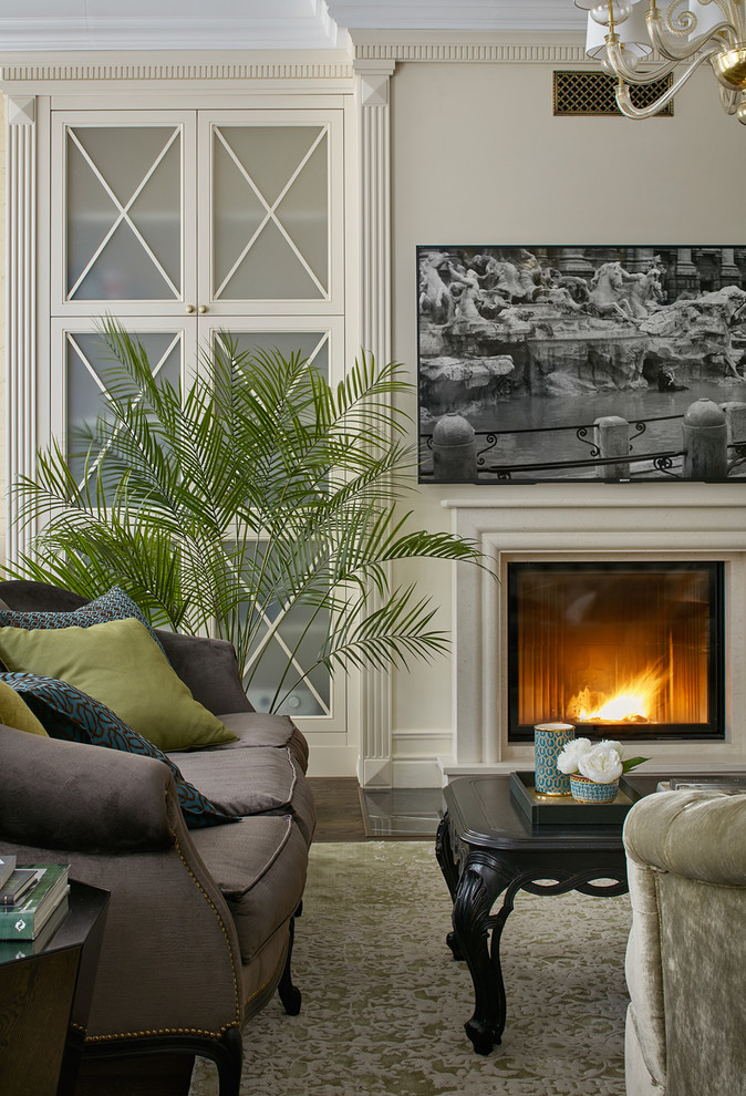 На фото: большая открытая гостиная комната в стиле неоклассика (современная классика) с бежевыми стенами, темным паркетным полом, стандартным камином, фасадом камина из камня и телевизором на стене