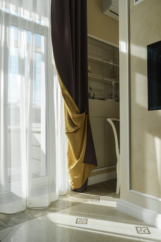 На фото: открытая гостиная комната в классическом стиле с бежевыми стенами, полом из керамогранита, телевизором на стене и бежевым полом