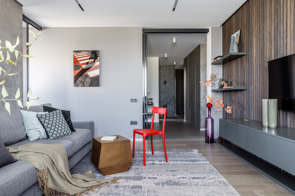 На фото: гостиная комната в современном стиле с серыми стенами, светлым паркетным полом, телевизором на стене и бежевым полом с