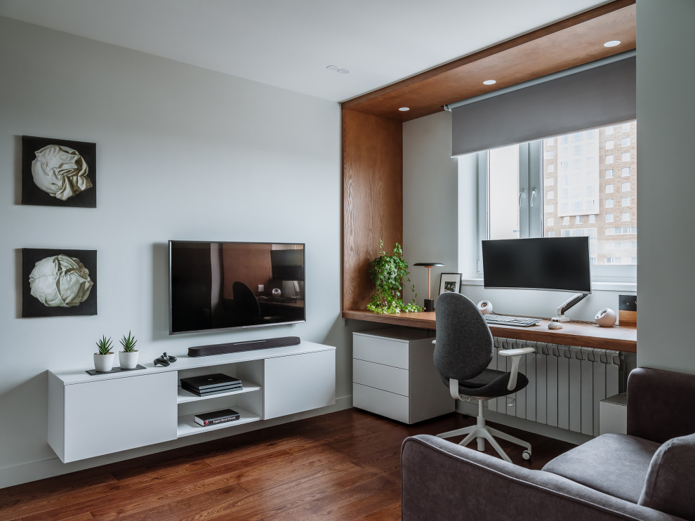 Modern inredning av ett vardagsrum, med vita väggar, mörkt trägolv, en väggmonterad TV och brunt golv