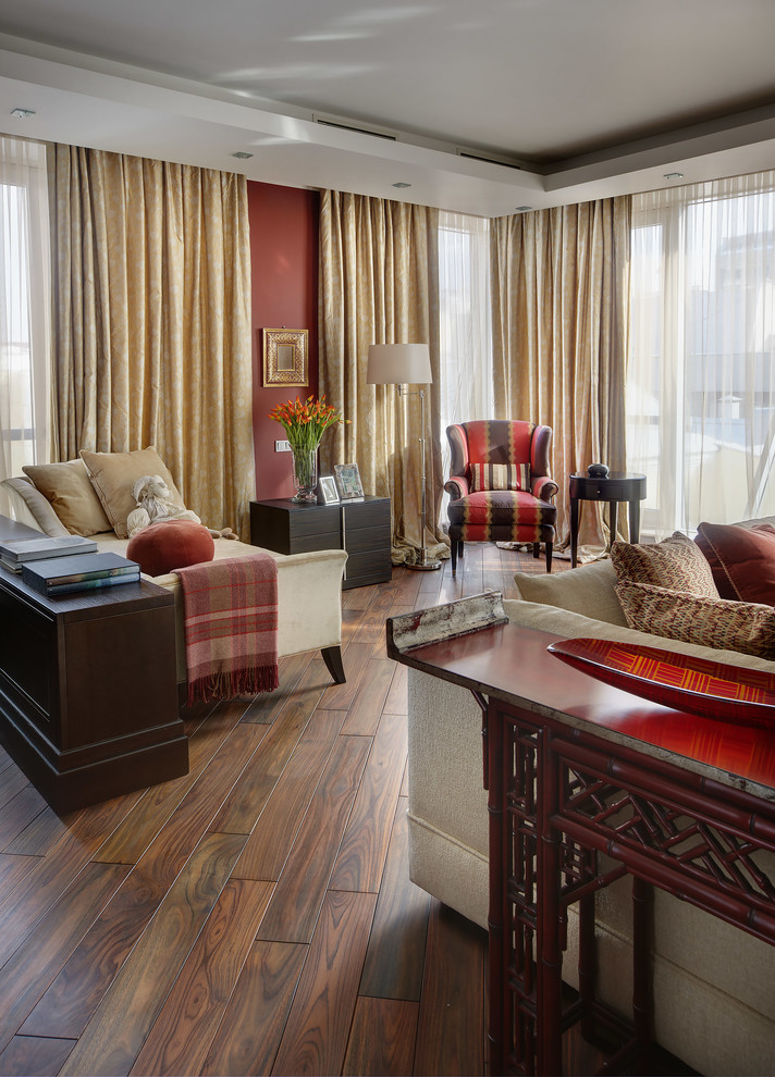 На фото: большая гостиная комната в стиле неоклассика (современная классика) с красными стенами, темным паркетным полом и тюлем на окнах с