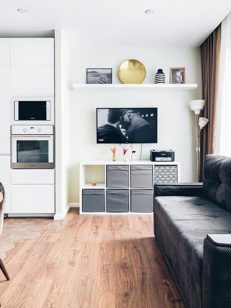 Свежая идея для дизайна: маленькая объединенная гостиная комната в скандинавском стиле с полом из ламината, телевизором на стене и коричневым полом для на участке и в саду - отличное фото интерьера