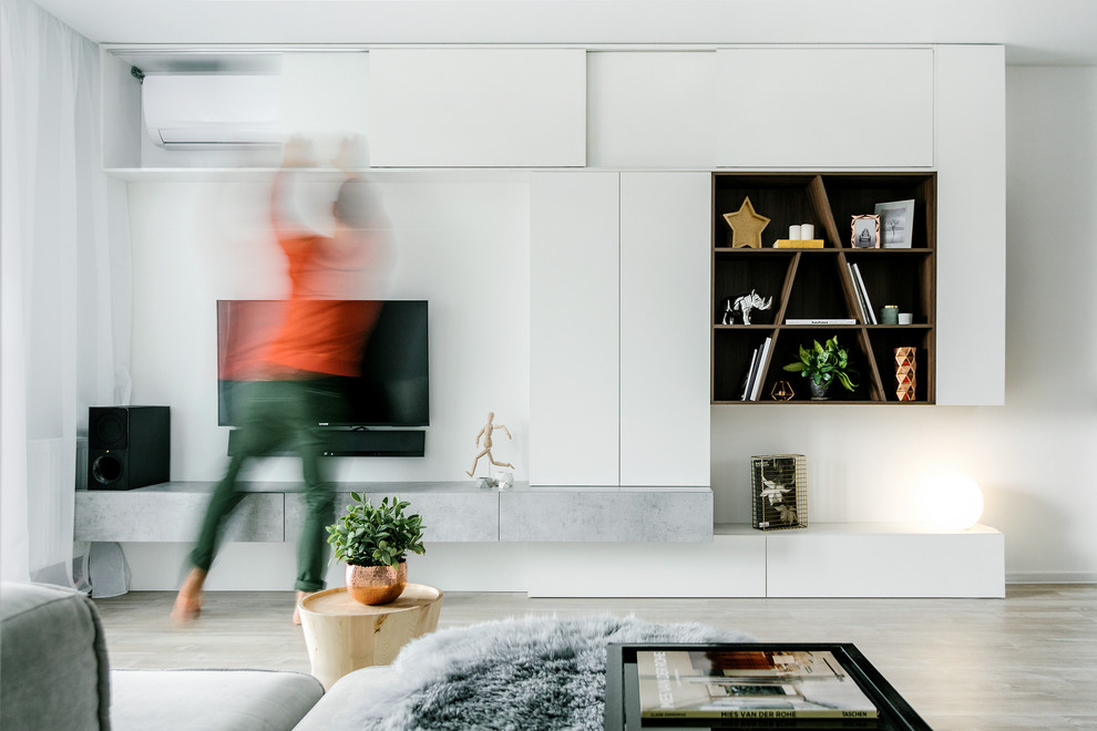 Modern inredning av ett vardagsrum, med vita väggar, ljust trägolv, en väggmonterad TV och beiget golv