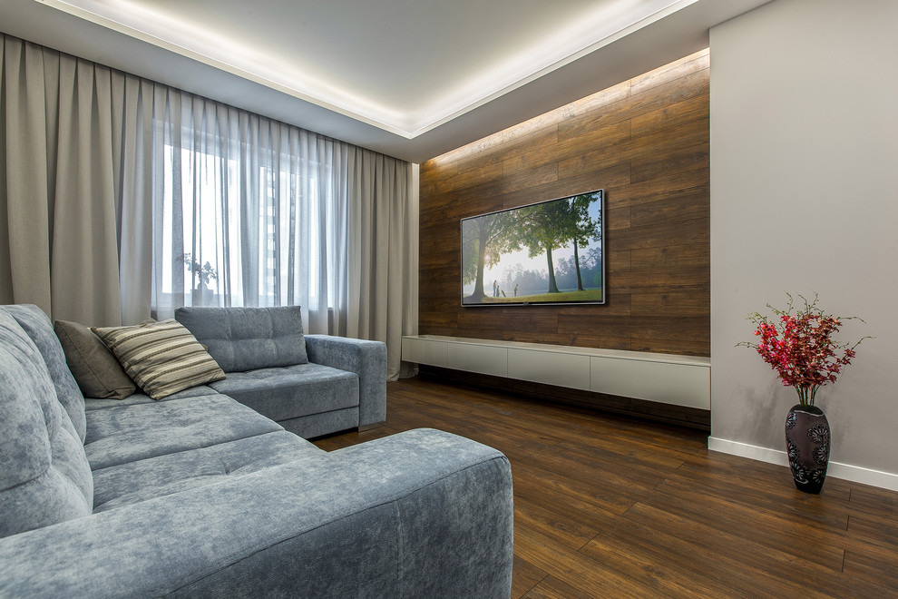 Стильный дизайн: гостиная комната в современном стиле с серыми стенами, темным паркетным полом и телевизором на стене - последний тренд