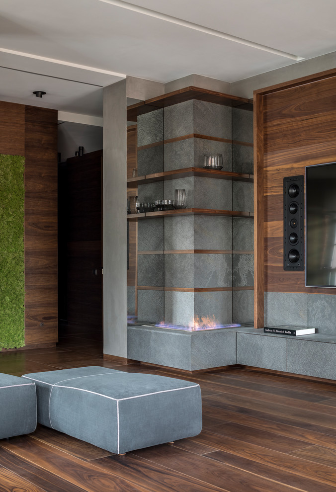 Diseño de salón para visitas abierto actual de tamaño medio con paredes grises, suelo de madera oscura, chimenea de esquina, pared multimedia y suelo marrón