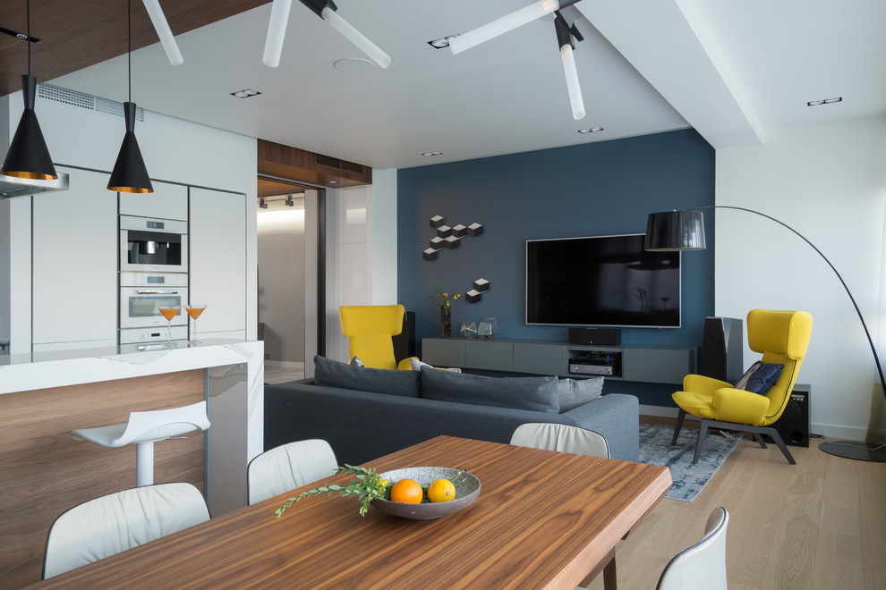Идея дизайна: открытая гостиная комната в современном стиле с синими стенами, светлым паркетным полом, телевизором на стене, бежевым полом, многоуровневым потолком, домашним баром и тюлем на окнах