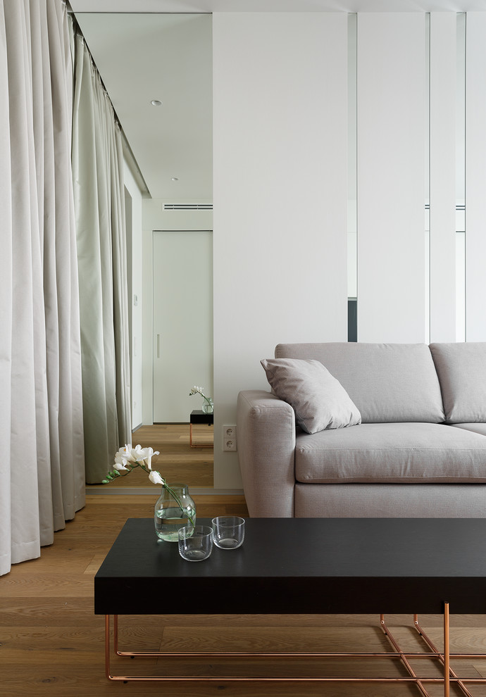 Immagine di un soggiorno minimal di medie dimensioni con pareti bianche, pavimento in legno massello medio, TV a parete e pavimento marrone
