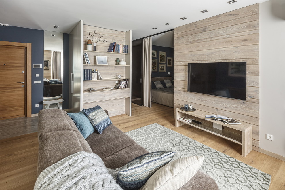 Modelo de salón para visitas abierto contemporáneo con paredes beige, suelo de madera clara, televisor colgado en la pared y suelo beige