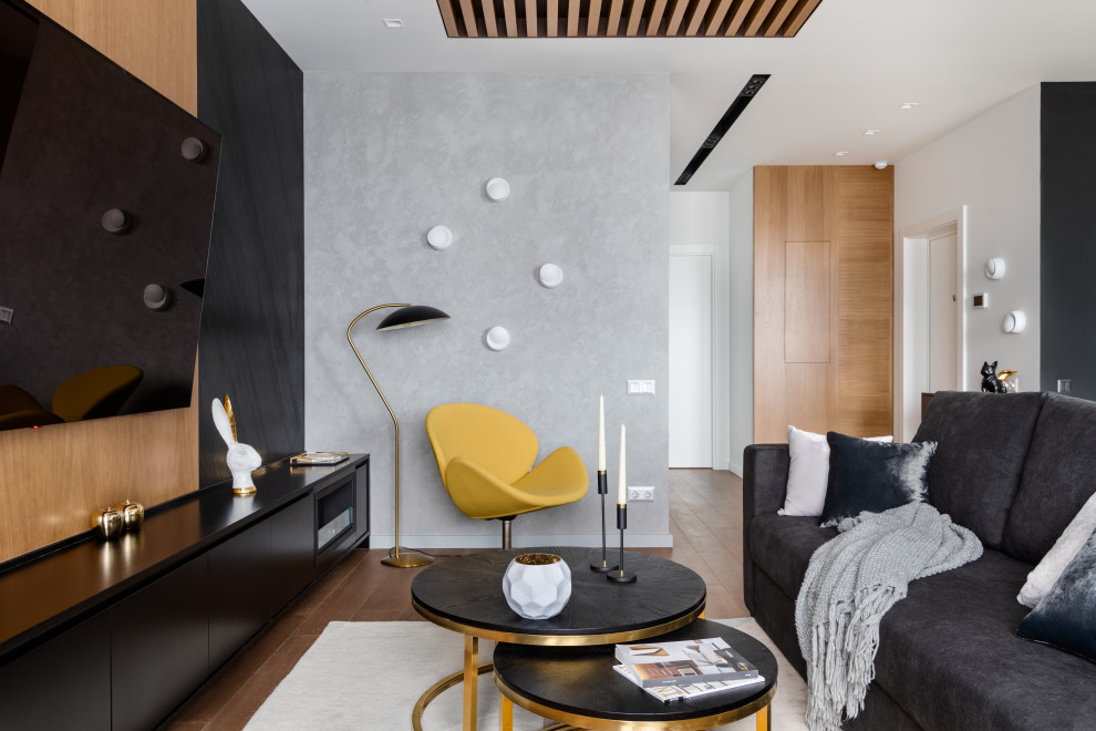 Modelo de salón abierto actual con paredes grises, suelo de madera clara, televisor colgado en la pared, suelo beige y madera