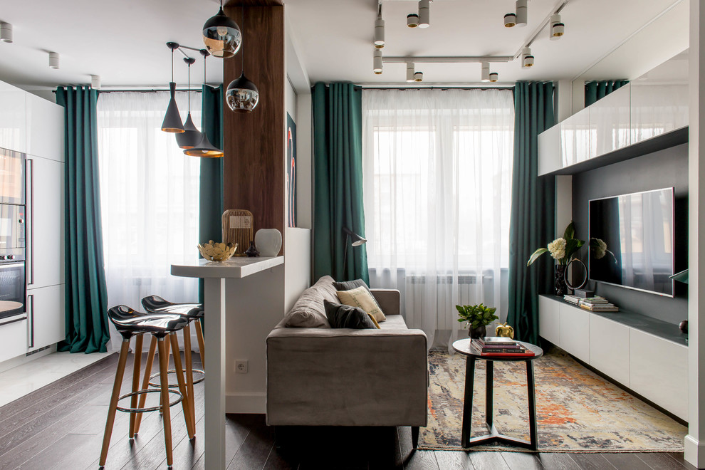 На фото: открытая, объединенная гостиная комната в современном стиле с белыми стенами, темным паркетным полом, телевизором на стене, коричневым полом и тюлем на окнах