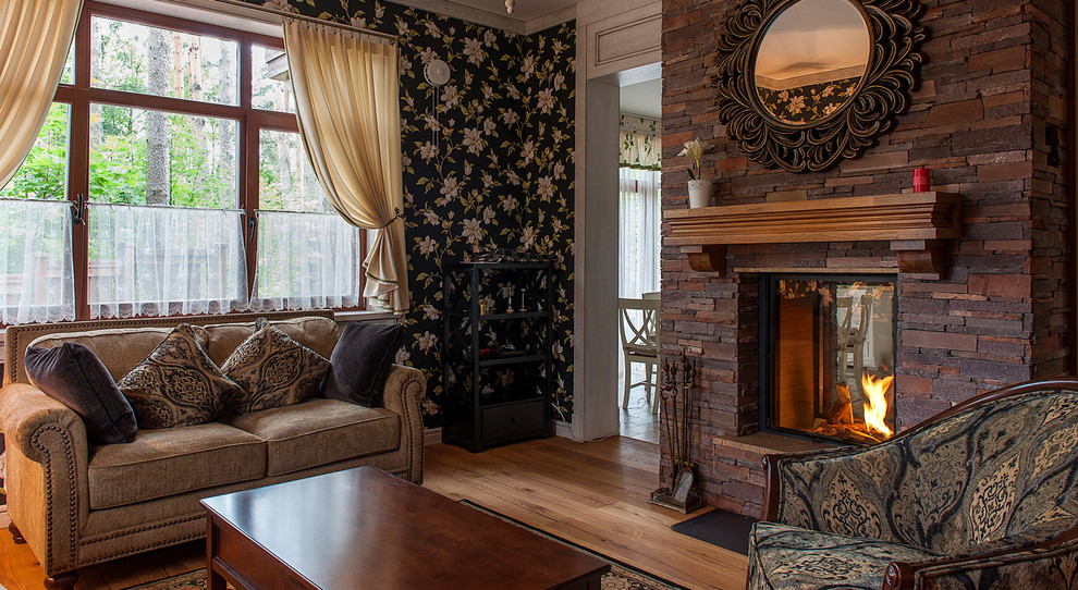 Ejemplo de salón para visitas abierto campestre con paredes negras, suelo de madera en tonos medios, chimenea de doble cara y marco de chimenea de piedra