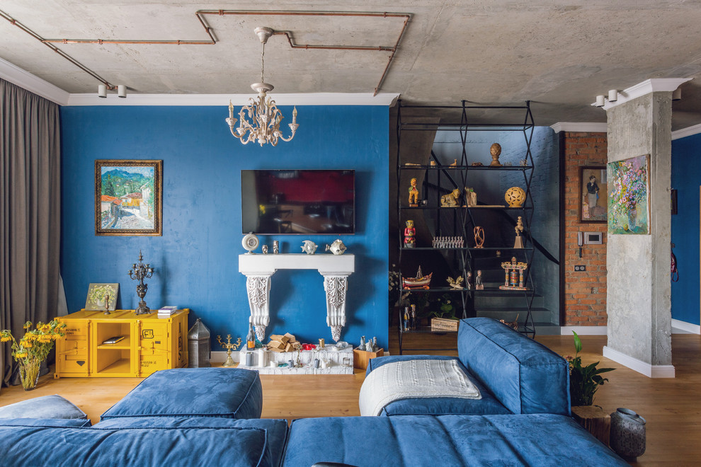 Стильный дизайн: открытая, объединенная гостиная комната в стиле лофт с паркетным полом среднего тона, коричневым полом, синими стенами, телевизором на стене и синим диваном - последний тренд
