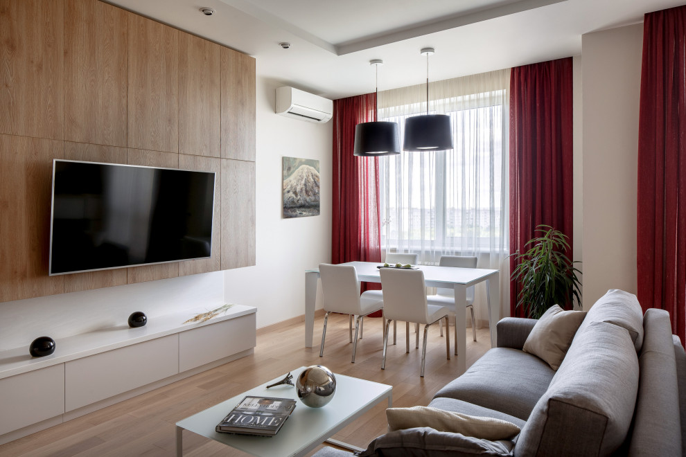 Стильный дизайн: изолированная, объединенная гостиная комната среднего размера в современном стиле с с книжными шкафами и полками, бежевыми стенами, паркетным полом среднего тона и телевизором на стене - последний тренд