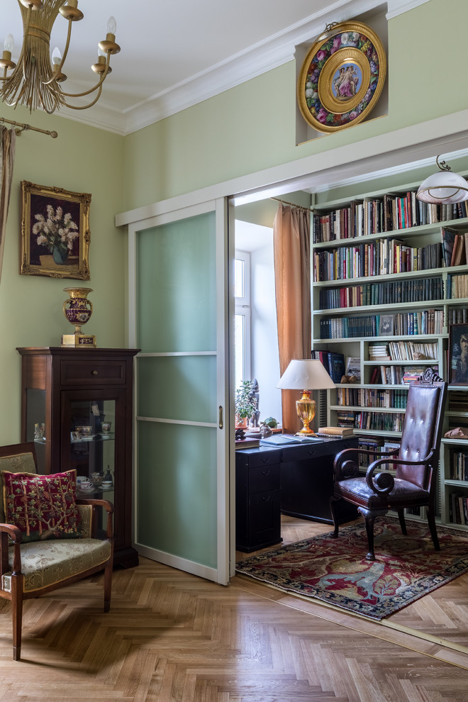 Ejemplo de sala de estar con biblioteca cerrada tradicional pequeña con paredes verdes y suelo de madera clara