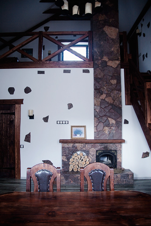 Imagen de sala de estar abierta rústica pequeña con paredes blancas, suelo de baldosas de cerámica, estufa de leña, marco de chimenea de piedra y televisor colgado en la pared