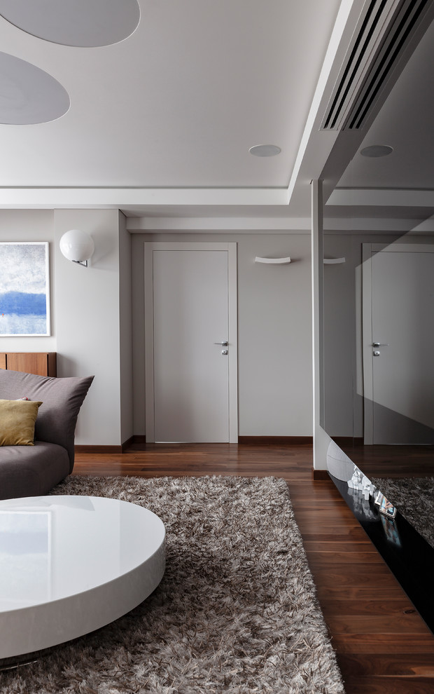 Foto de salón cerrado actual de tamaño medio con paredes grises, suelo de madera oscura, televisor retractable y suelo marrón